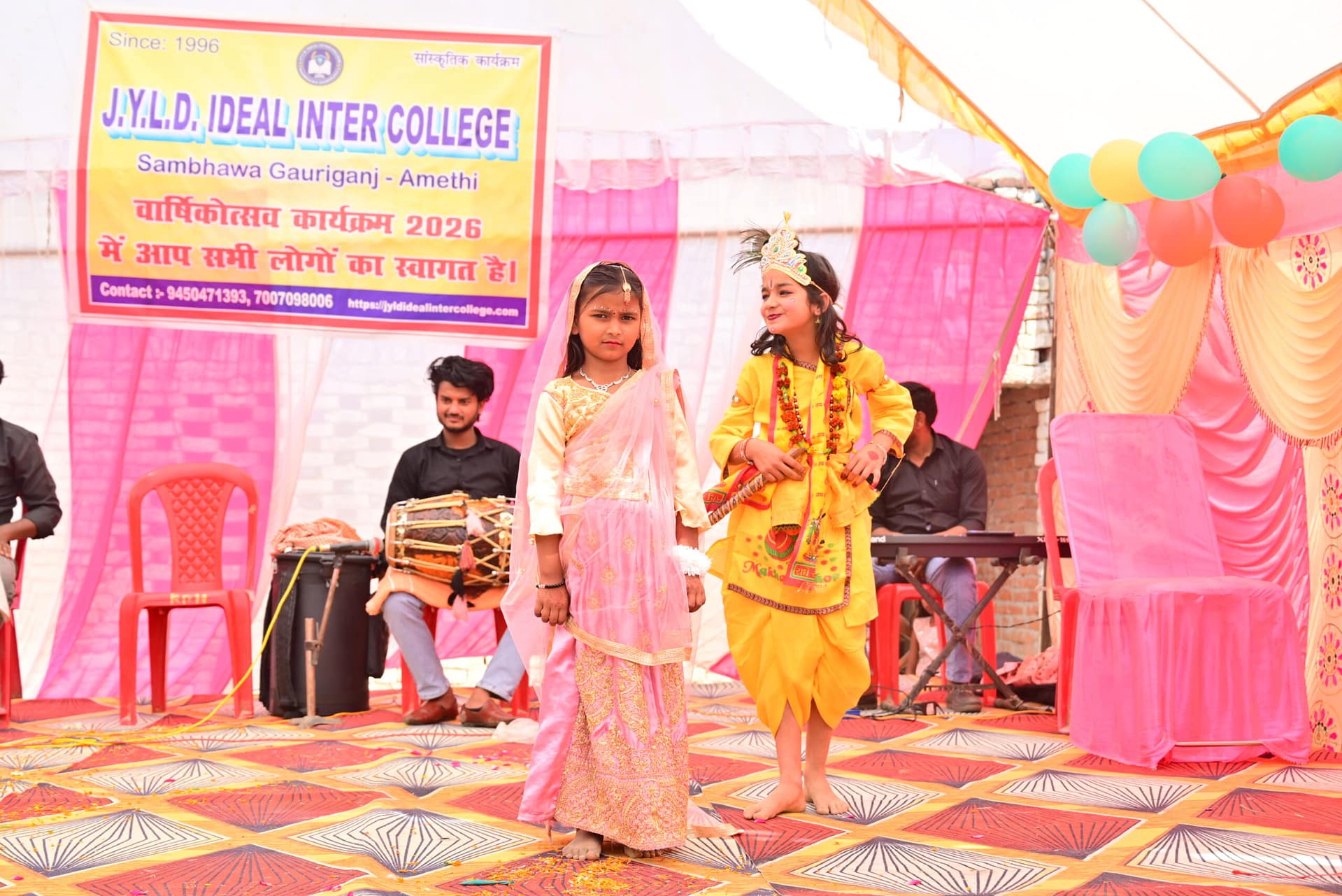 JYLD Ideal Inter College varshikotsav 2026 mein chhoti bachchiyan Radha Krishna ke vesh mein manch par natak prastuti dete hue dhol tabla sangat ke saath